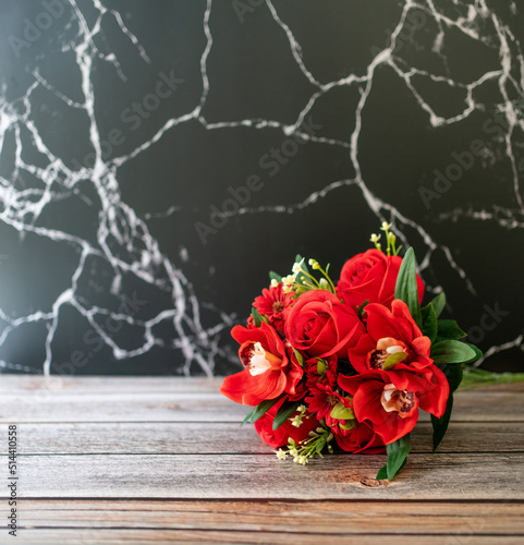 A bouquet of red roses on the wooden floor and with a marble wall in the background