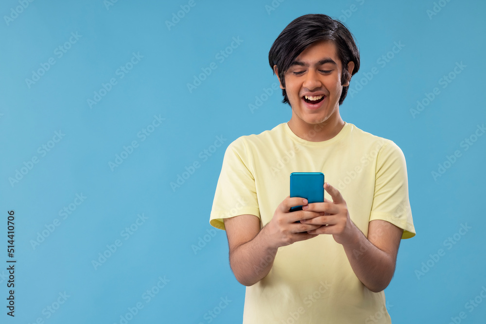 Portrait of a happy teenage boy using Smartphone while standing against blue background Portrait of a happy teenage boy using Smartphone while standing against blue background