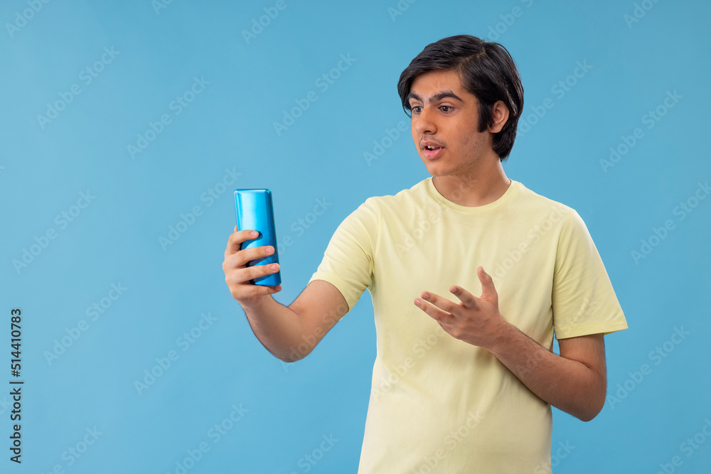 Teenage boy having video call on Smartphone against blue background Teenage boy having video call on Smartphone against blue background
