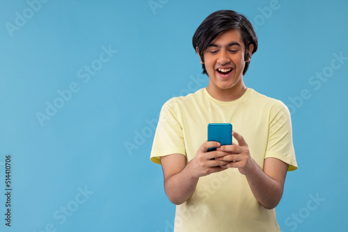 Portrait of a happy teenage boy using Smartphone while standing against blue background