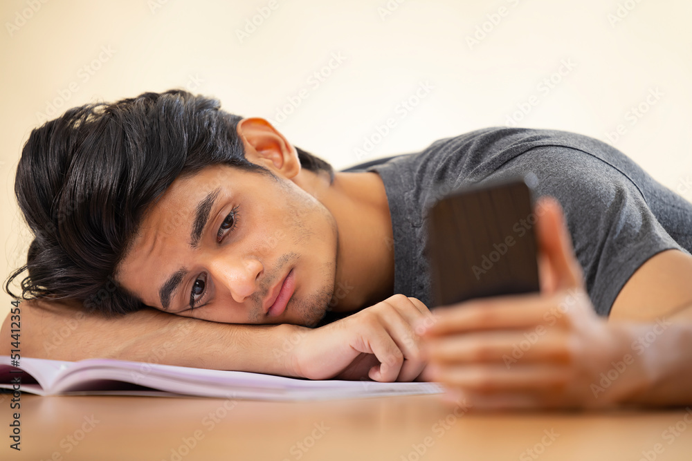 Close-up portrait of a tired teenager leaning head on hand with holding a smartphone Close-up portrait of a tired teenager leaning head on hand with holding a smartphone
