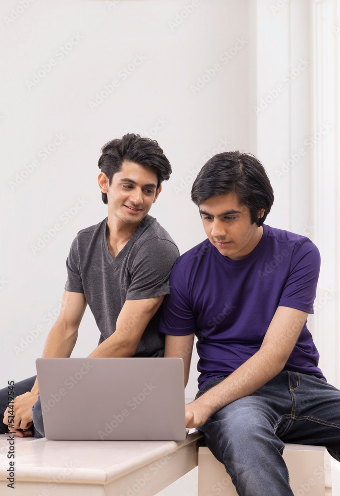 Portrait of two teenage boys using laptop against plain background Portrait of two teenage boys using laptop against plain background