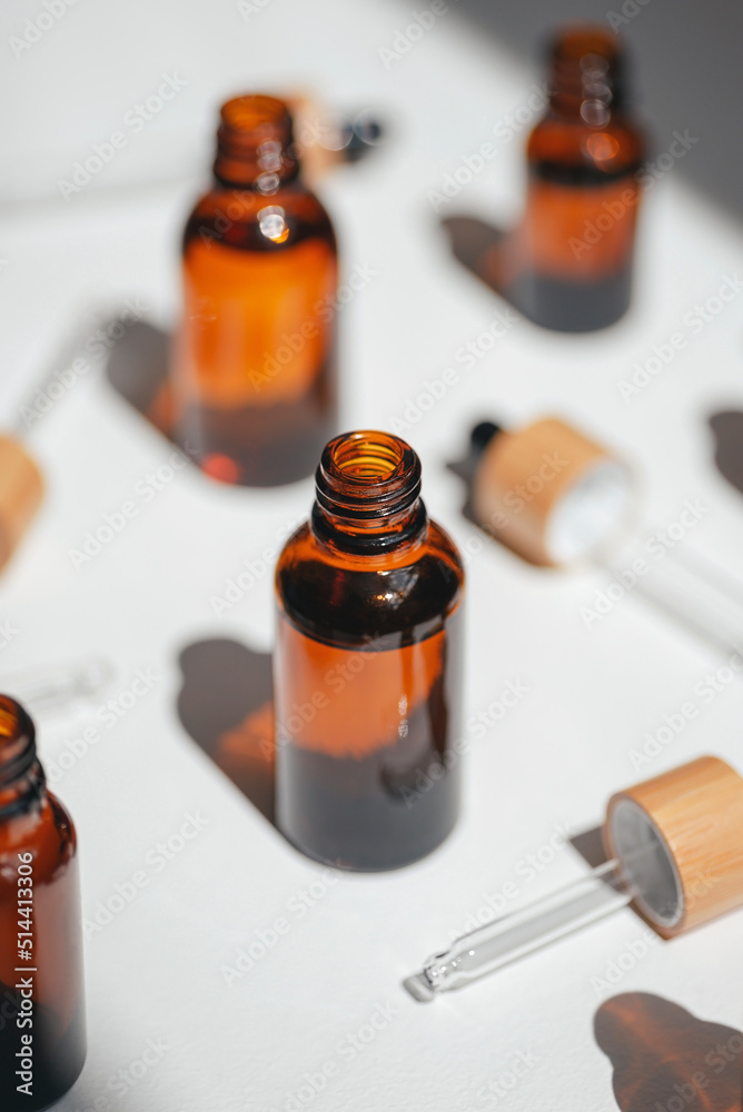 Open amber, blue and transparent bottles without cap with serum or essential oil with white flowers. Beige background with daylight and beautiful shadows. Beauty concept for face and body care Open amber, blue and transparent bottles without cap with serum or essential oil with white flowers. Beige background with daylight and beautiful shadows. Beauty concept for face and body care