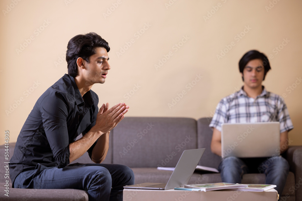 Two happy teenage boys doing homework at home using laptop Two happy teenage boys doing homework at home using laptop