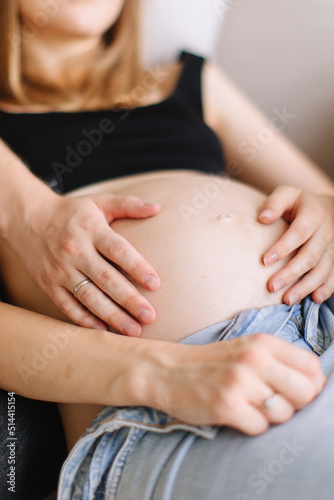 A pregnant girl with blond hair in unbuttoned jeans lies, and her husband touches her pregnant belly. © Viktor