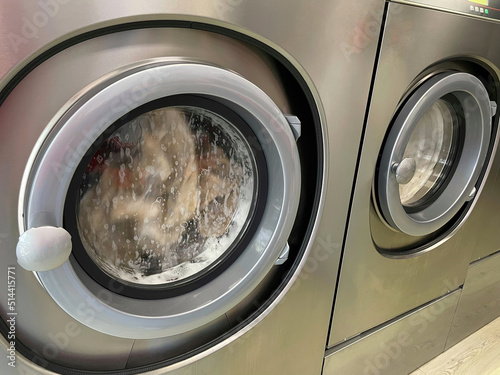 Dirty clothes spinning inside the main doors of two stainless steel industrial washing machines. © cjsolanop