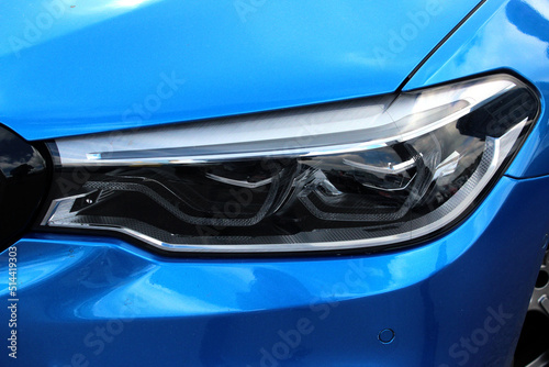  Modern sedan front headlight with headlight washer. Blue car headlight.