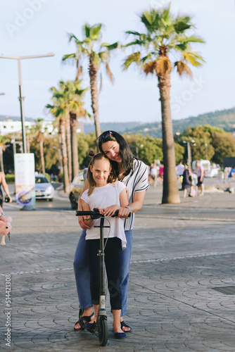 Happy family lifestyle and holiday concept. Mother  little boy  girl   riding scooters  walking in old city  street. Laughing on a summer sunny day. Having fun