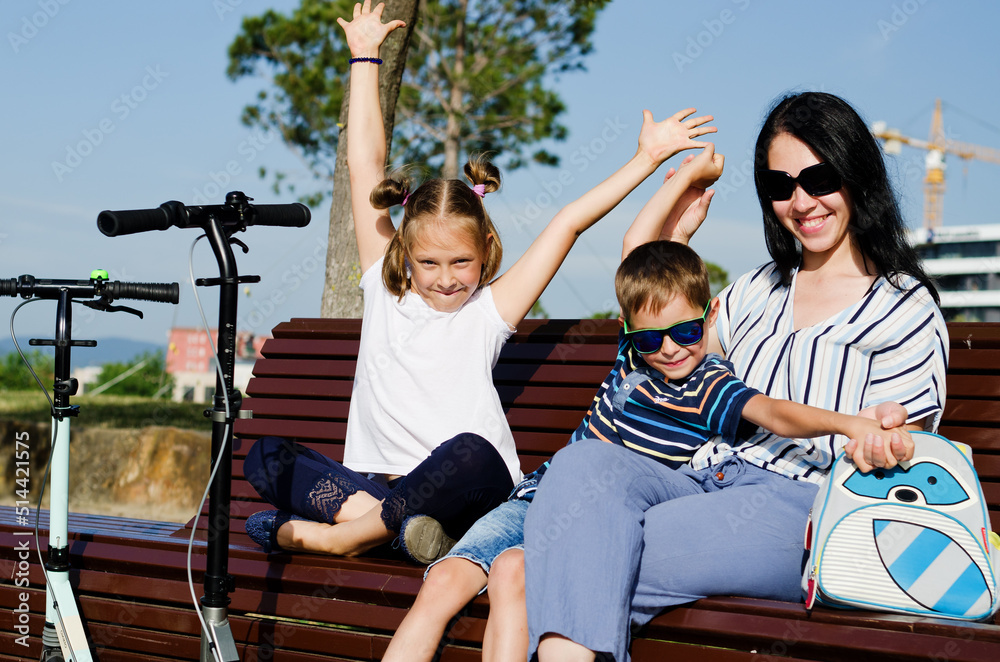 Obraz premium Happy family lifestyle and holiday concept. Mother, little boy, girl , riding scooters, walking in old city, street. Laughing on a summer sunny day. Having fun