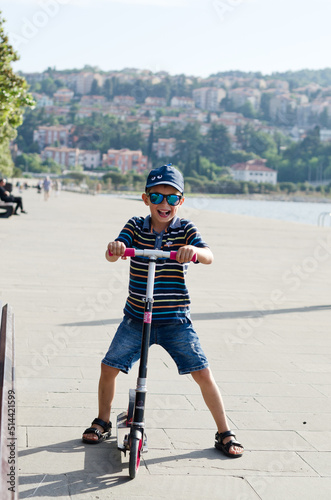Fototapeta Naklejka Na Ścianę i Meble -  Happy family lifestyle and holiday concept. little boy riding scooter, walking in old city, street. Laughing on a summer sunny day. Having fun