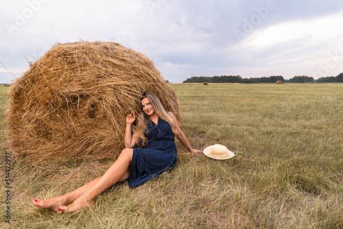 Girl and haystack. Smiling blonde woman in a polka-dot dress sitting on the grass next to a haystack. Harvest concept ,copy space photo