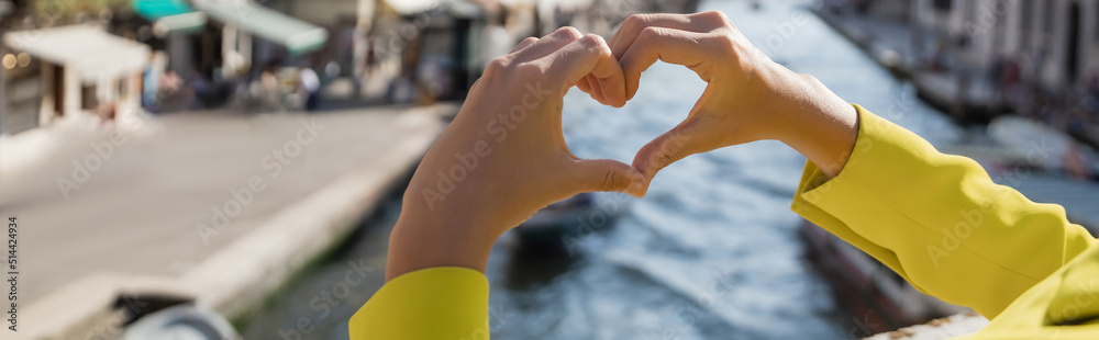 cropped view of woman showing heart symbol on blurred background in Venice, banner. cropped view of woman showing heart symbol on blurred background in Venice, banner.