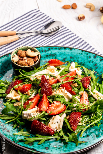 Fresh strawberry salad with arugula, strawberries and cheese brie, camembert. Plate with a keto diet food. Delicious breakfast or snack on a light background, top view