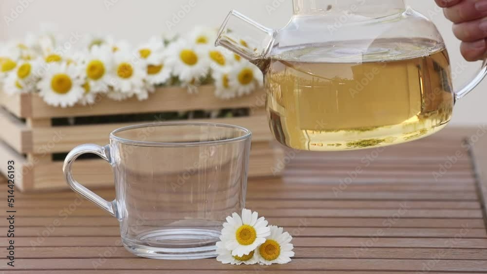 Closeup hd video of woman's hand pours chamomile herbal tea into a cup from a glass transparent teapot against the background of a basket with chamomile flowers Closeup hd video of woman's hand pours chamomile herbal tea into a cup from a glass transparent teapot against the background of a basket with chamomile flowers