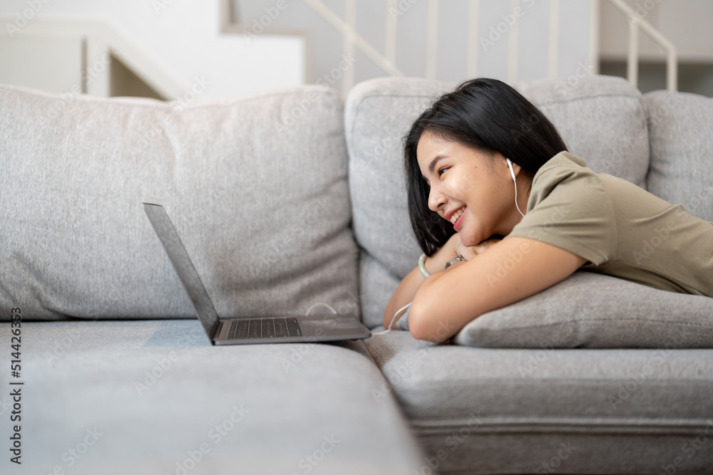 Relaxed woman using laptop in living room, enjoying working, internet shopping, checking social network, reading news or communicating online with computer laying on sofa Relaxed woman using laptop in living room, enjoying working, internet shopping, checking social network, reading news or communicating online with computer laying on sofa
