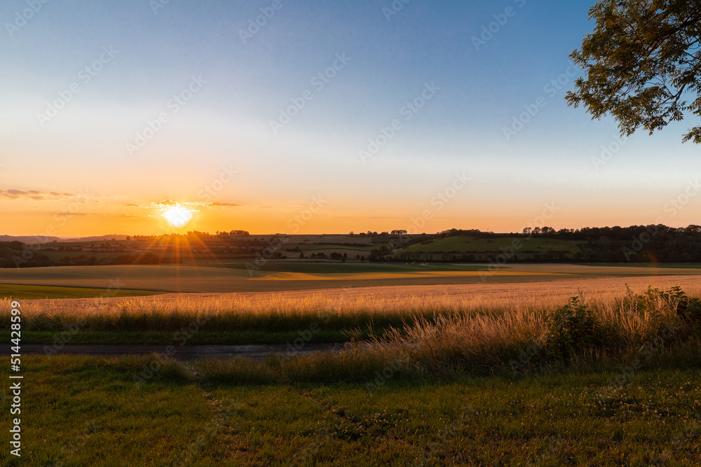 Sunset over the rolling hills in Elkenrade in the of south Limburg in the Netherlands with a spectacular view over the fields, full of wheat and some amazing beams from the sun during golden hour.