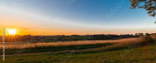Sunset over the rolling hills in Elkenrade in the of south Limburg in the Netherlands with a spectacular view over the fields, full of wheat and some amazing beams from the sun during golden hour. © KimWillems