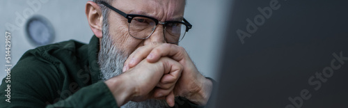 stressed senior man in eyeglasses frowning and covering face with clenched hands, banner. photo