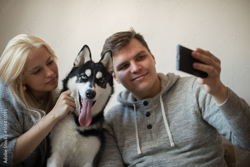 Happy young couple taking a selfie together with dog on the couch at home