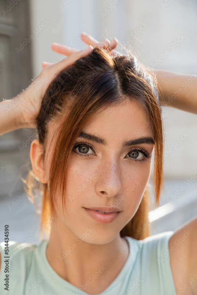 close up portrait of charming woman fixing red hair and looking at camera outdoors. close up portrait of charming woman fixing red hair and looking at camera outdoors.