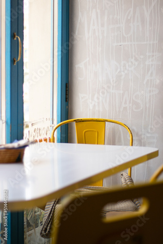 Bright mexican cafe interior. White table, yellow metal vintage chairs. Jute basket with napkins and cultery on the table. Restaurant furniture