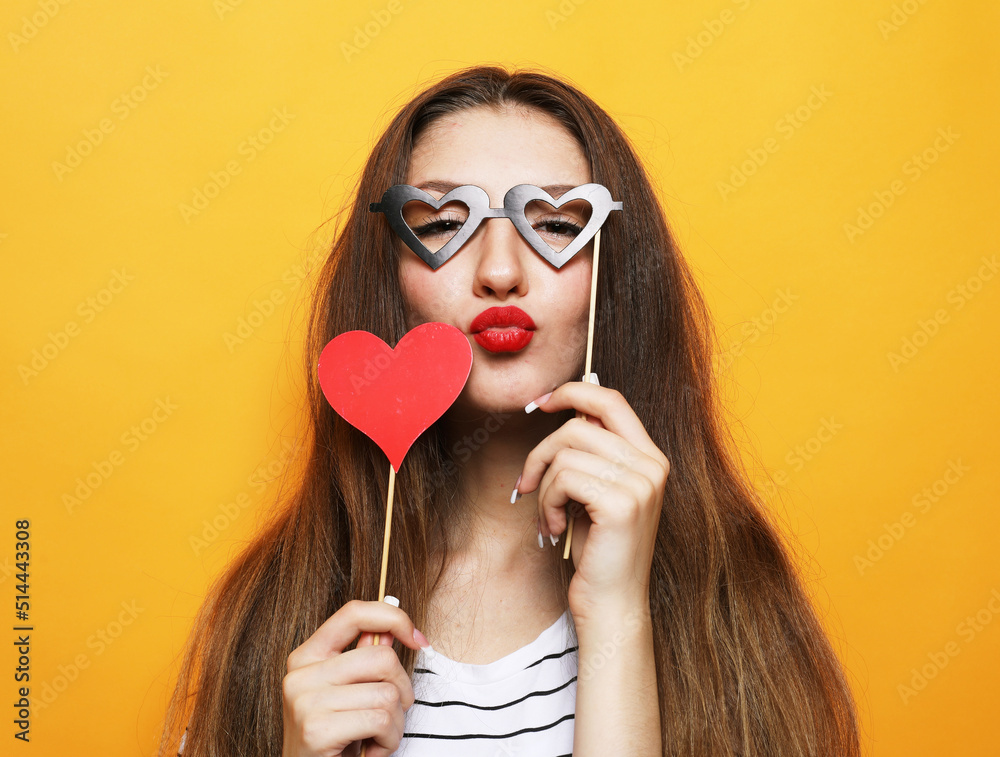 Playful young woman holding a party glasses over yellow background. Playful young woman holding a party glasses over yellow background.
