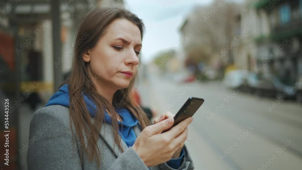 Woman stands at a public transport stop and checks the timetable. Tram pulls up in the background. Woman stands at a public transport stop and checks the timetable. Tram pulls up in the background.