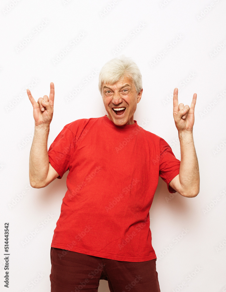 Old man wearing casual red t-shirt standing over isolated white background shouting with crazy expression doing rock symbol with hands up. Old man wearing casual red t-shirt standing over isolated white background shouting with crazy expression doing rock symbol with hands up.