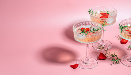 Boozy Refreshing Rose Wine, strawberry cocktail or mocktail, refreshing summer drink with champagne, strawberries, ice cubes and rosemary on pink background