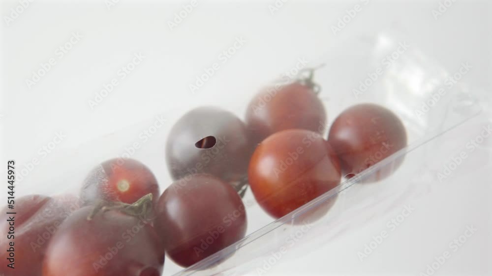 Organic black cocktail tomatoes in a plastic box on a white background. Organic black cocktail tomatoes in a plastic box on a white background.