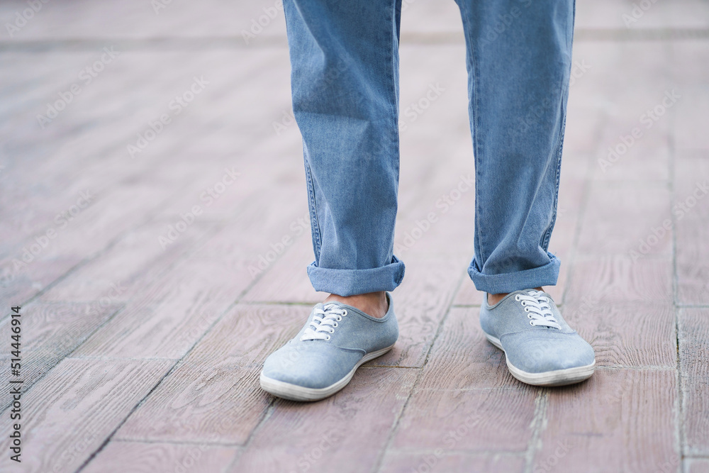 Stylish man feet in denim jeans and sneakers shoes standing alone outdoors on street marble or ceramic plate