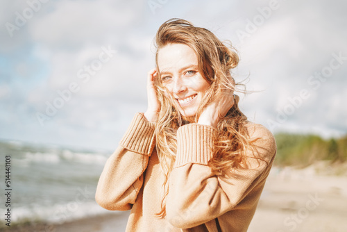 Young beautiful woman with long hair in beige sweater enjoying life on sea beach on sunset