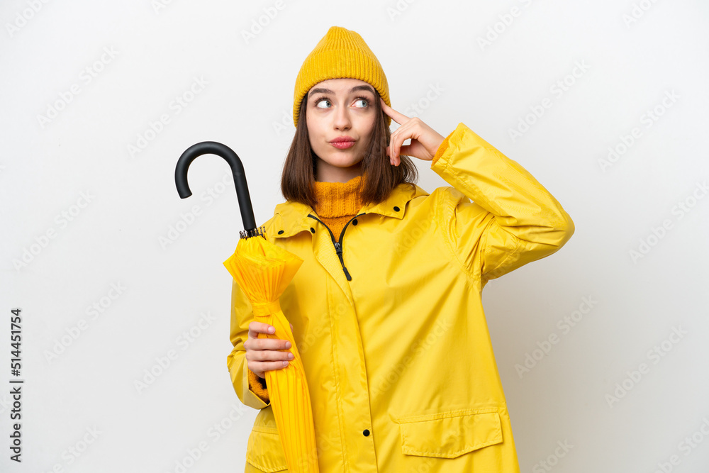 Young Ukrainian woman with rainproof coat and umbrella isolated on white background having doubts and thinking Young Ukrainian woman with rainproof coat and umbrella isolated on white background having doubts and thinking