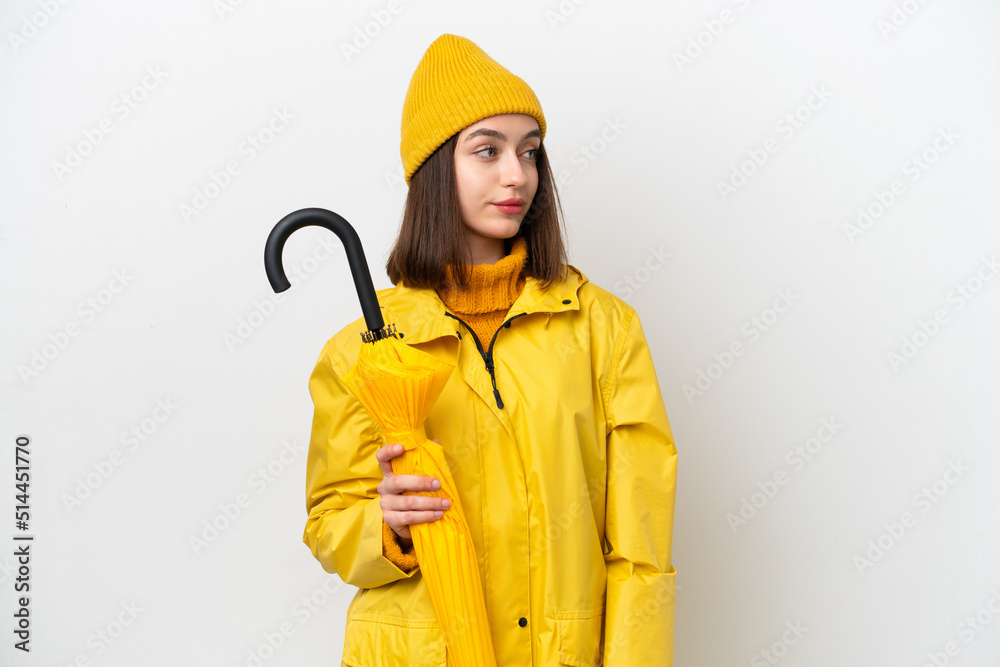 Young Ukrainian woman with rainproof coat and umbrella isolated on white background looking to the side Young Ukrainian woman with rainproof coat and umbrella isolated on white background looking to the side