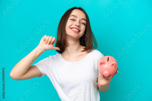 Young Ukrainian woman holding a piggybank isolated on blue background proud and self-satisfied