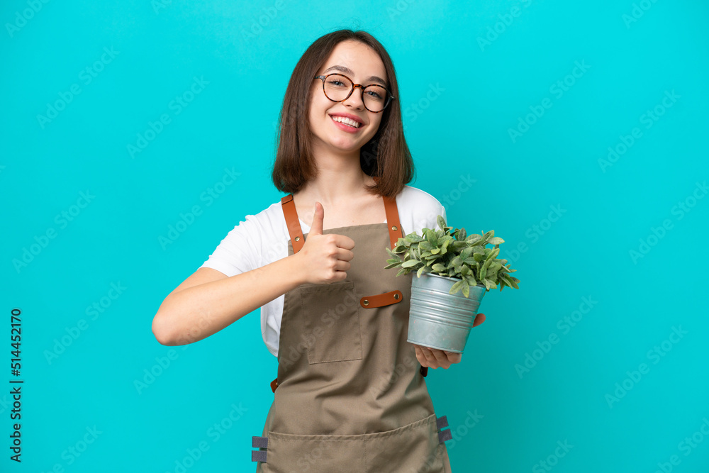 Gardener Ukrainian woman holding a plant isolated on blue background giving a thumbs up gesture Gardener Ukrainian woman holding a plant isolated on blue background giving a thumbs up gesture