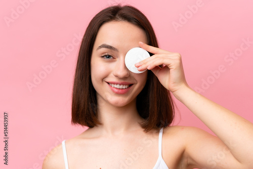 Young Ukrainian woman isolated on pink background with cotton pad for removing makeup from her face and smiling