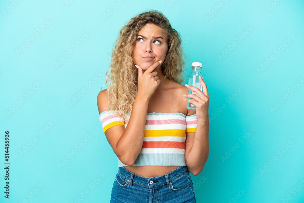 Young blonde woman with a bottle of water isolated on blue background having doubts Young blonde woman with a bottle of water isolated on blue background having doubts