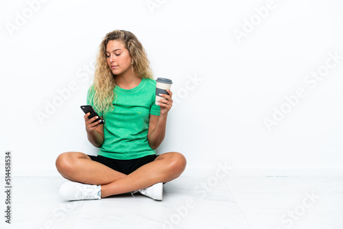 Girl with curly hair sitting on the floor holding coffee to take away and a mobile