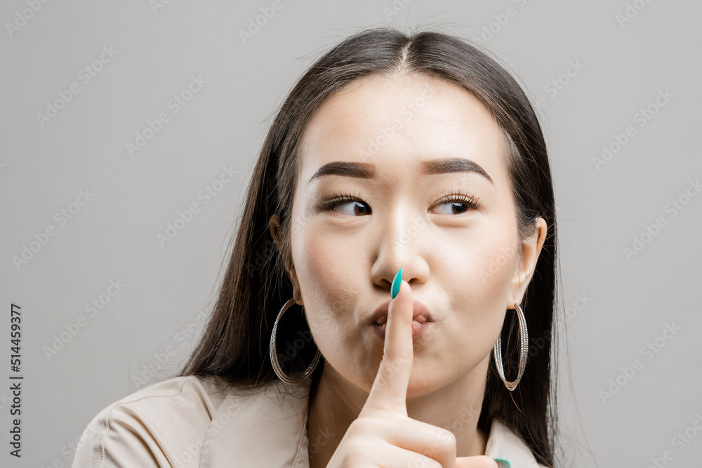 Portrait of a asian girl on a light background. Asian woman showing silence gesture Portrait of a asian girl on a light background. Asian woman showing silence gesture