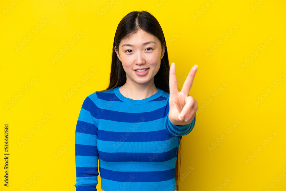 Young Chinese woman isolated on yellow background smiling and showing victory sign Young Chinese woman isolated on yellow background smiling and showing victory sign