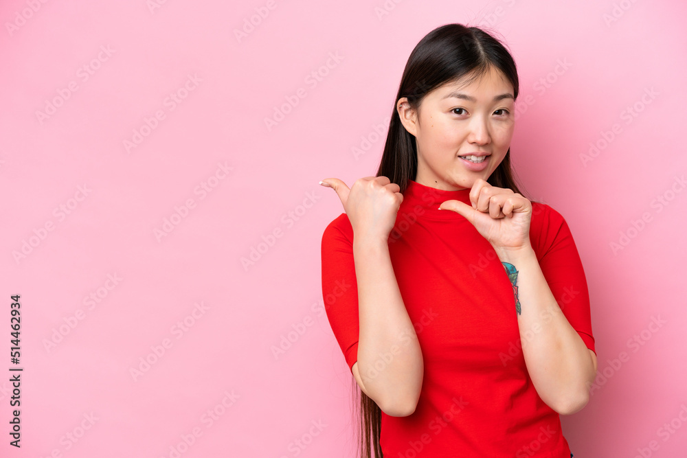 Young Chinese woman isolated on pink background pointing to the side to present a product Young Chinese woman isolated on pink background pointing to the side to present a product