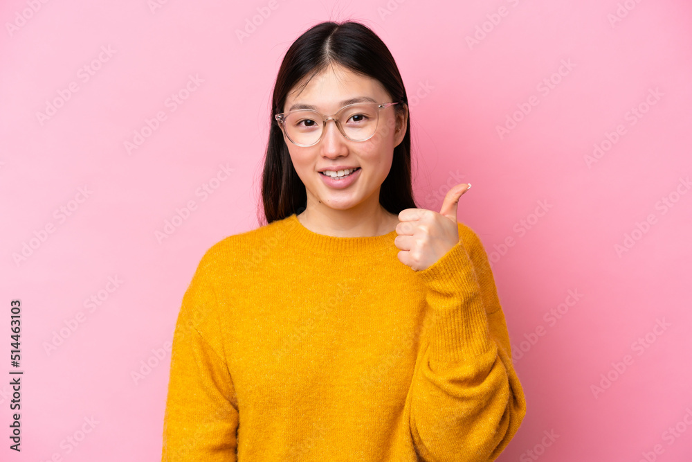 Young Chinese woman isolated on pink background With glasses and with thumb up