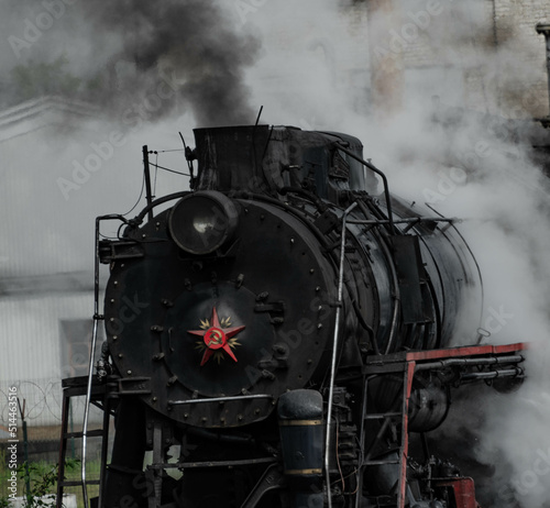 an old vintage steam locomotive in close-up with a red star on the nose covered in huge clouds of steam and smoke