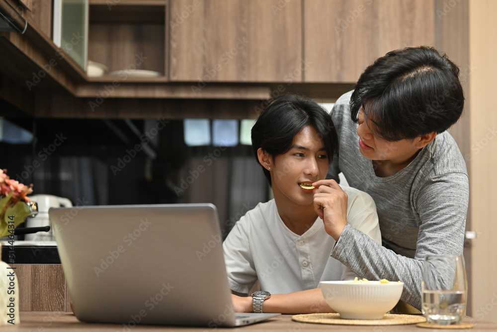 Happy gay couple spending the day together with the movie on the laptop while a man feeding his beloved partner, LGBT couple lifestyle, Relationships and equality concept. Happy gay couple spending the day together with the movie on the laptop while a man feeding his beloved partner, LGBT couple lifestyle, Relationships and equality concept.