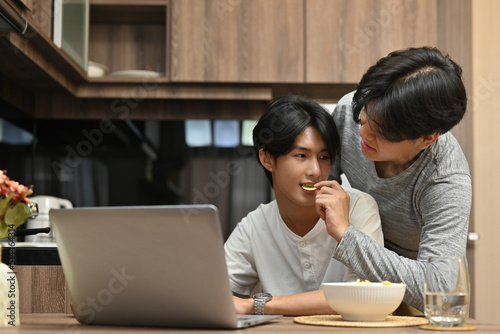 Happy gay couple spending the day together with the movie on the laptop while a man feeding his beloved partner  LGBT couple lifestyle  Relationships and equality concept.