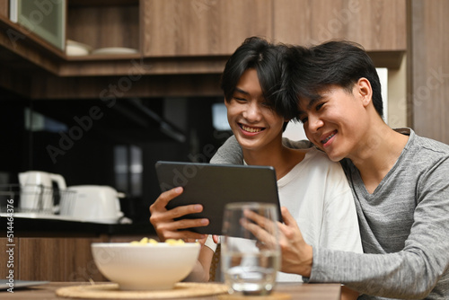 Asian LGBT couple having an enjoy moment with their digital tablet with kitchen as the background  LGBT couple lifestyle  Relationships and Equality concept.