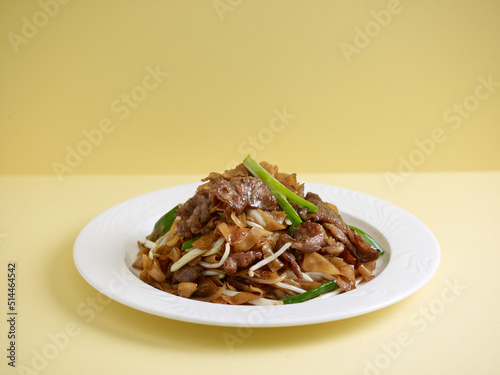 wok-fried Hor Fun with sliced beef served in a dish isolated on wooden board side view on grey background photo