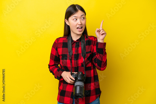 Young photographer Chinese woman isolated on yellow background intending to realizes the solution while lifting a finger up