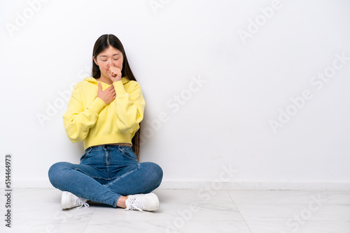 Young Chinese woman sitting on the floor isolated on white wall is suffering with cough and feeling bad